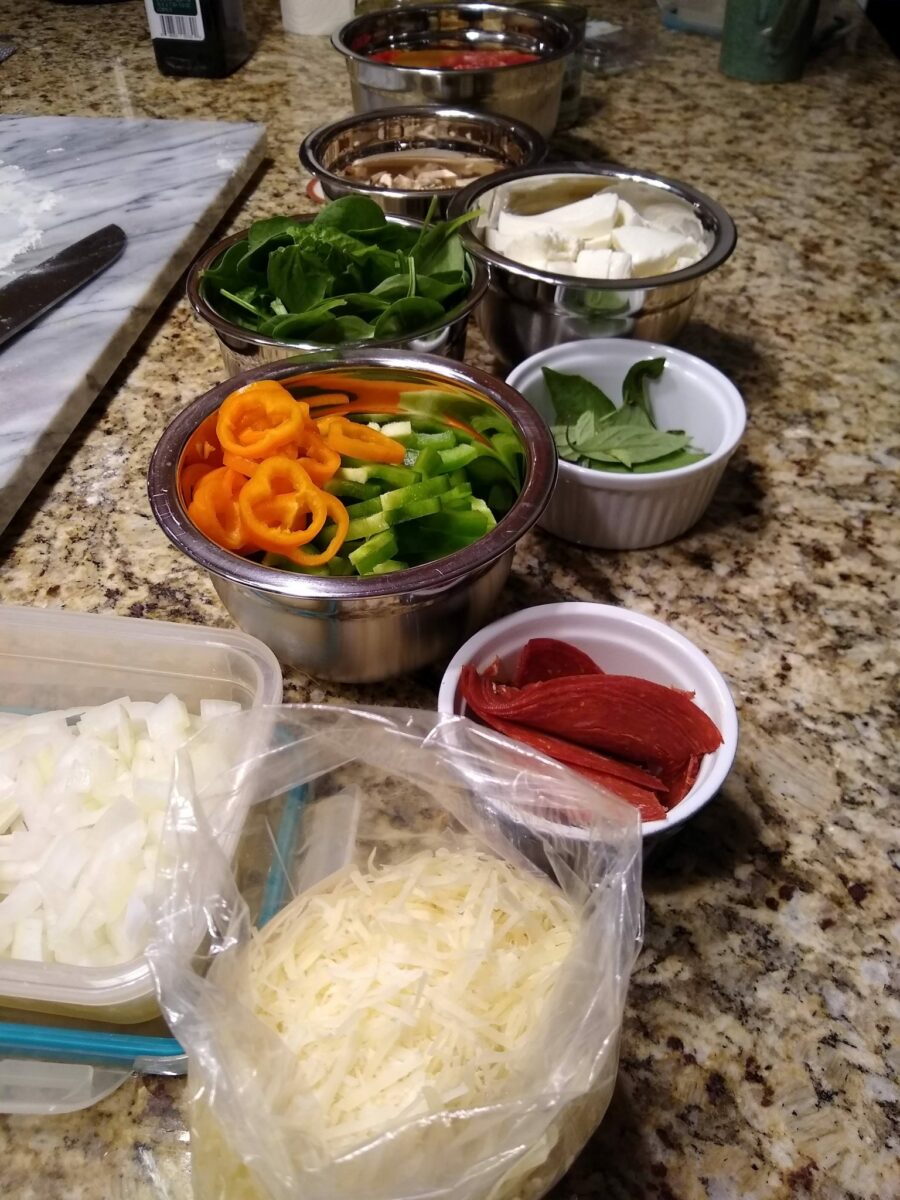 Several bowls of different sizes containing different pizza toppings