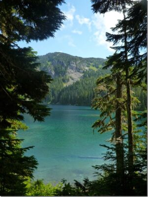Mowich Lake in Mt Rainier National Park is the trailhead for the Spray Park trail. It is a turquoise blue color, surrounded by forested hillsides.