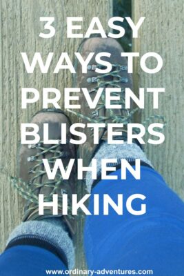 Two worn hiking boots seen from the person wearing them. A person's lower legs with blue leggings and gray and blue socks are also visible. The person is standing on a wooden path. Text reads: 3 easy ways to prevent blisters when hiking