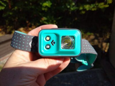 A headlamp is an important thing I pack for a hike. This headlamp is blue green and is being held in someone's hand with the light facing the camera