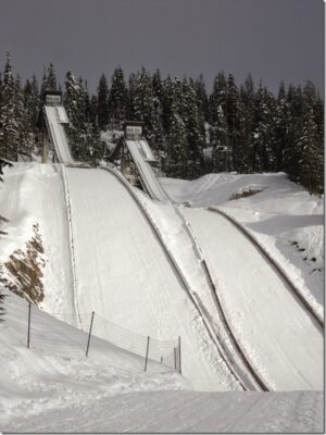 Two very high ski jumps covered in snow are surrounded by forest at Whistler olympic park.