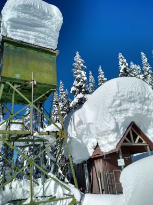 A communications tower covered in many feet of snow in the forest along the trail