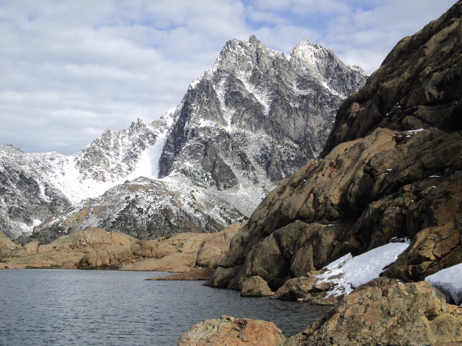 A high mountain rises behind rocks surrounding an alpine lake on a cloudy day at Lake Ingalls, one of the best hikes in Washington