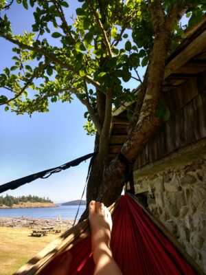 A person's foot is in a hammock in the shade near a Washington beach, spencer spit on Lopez Island