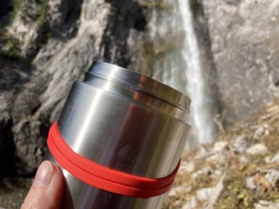 A stainless steel food container being held up in front of a waterfall