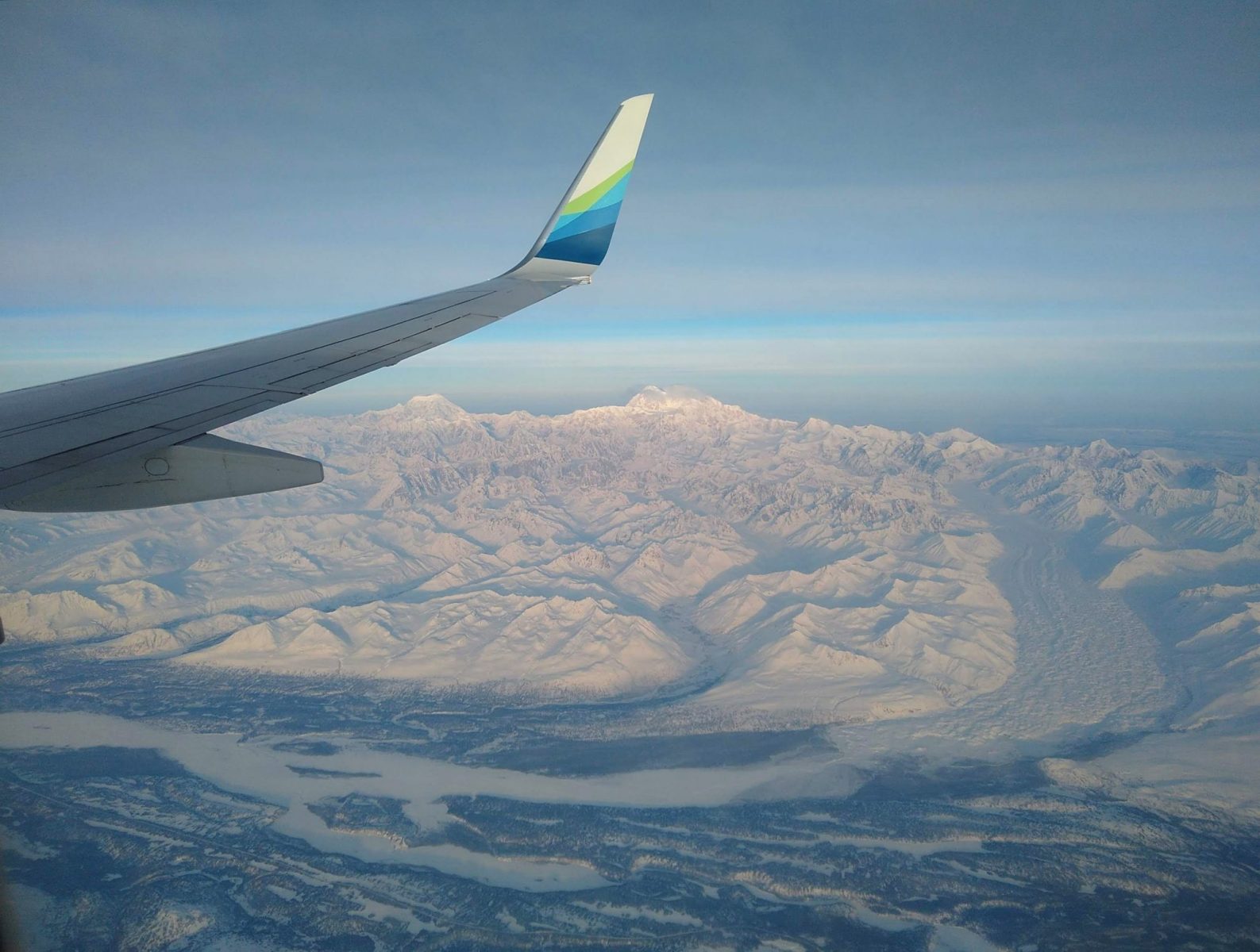 Denali National Park below the wing of an airplane. There are mountains, glaciers and a river valley
